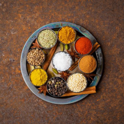 Mix spices on round metal plate - coriander seeds, ground red pepper, salt, black pepper, rosemary, turmeric, curry. Top view, close up, metall rusty background.